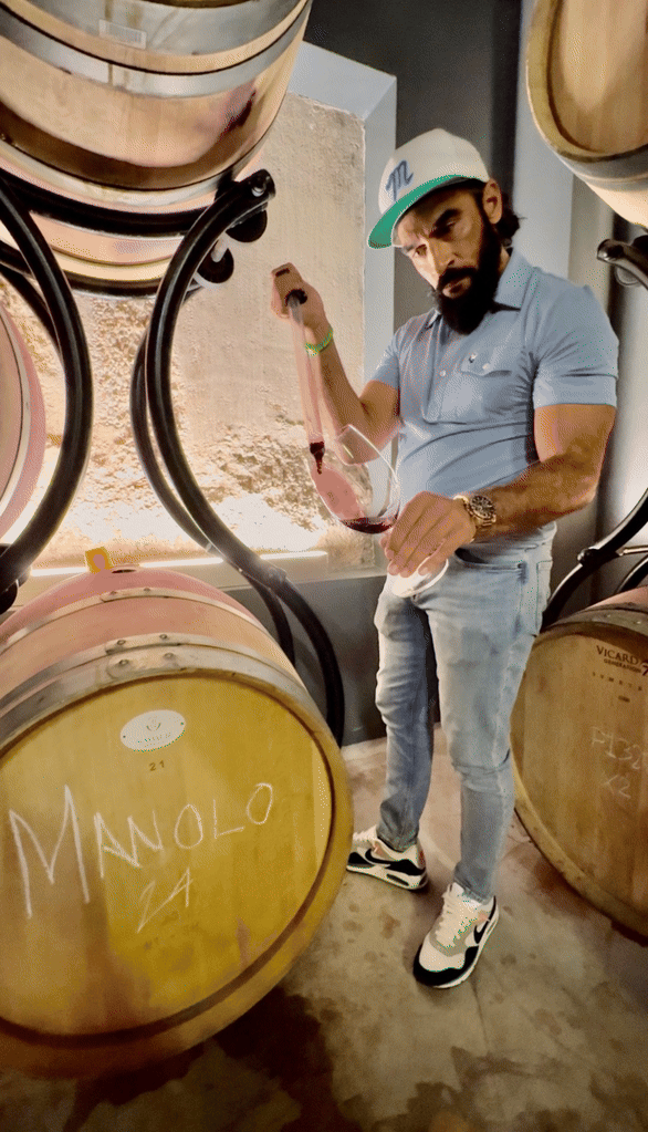 Manolo filling a glass with red wine in the barrel room